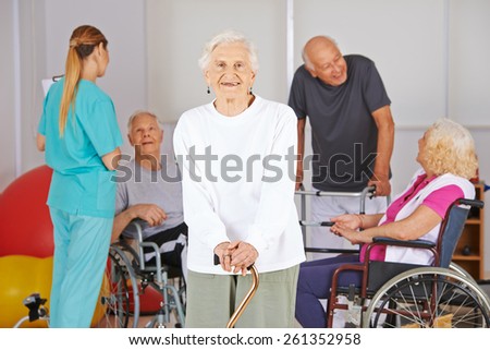 Smiling old woman standing in front of group of senior people in nursing home