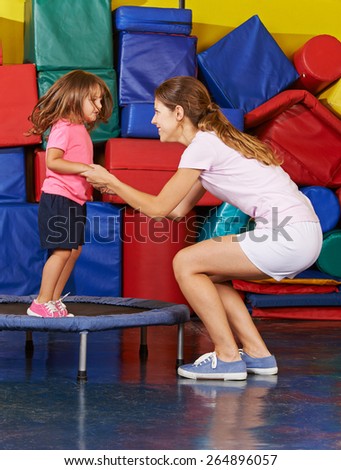 Girl jumping on trampoline with nursery teacher during children sports