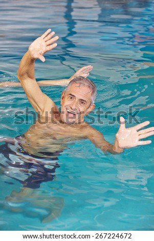 Elderly man playing water ball in swimming pool with his hands reaching out