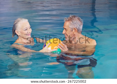 Happy senior couple playing water ball with beach ball in swimming pool