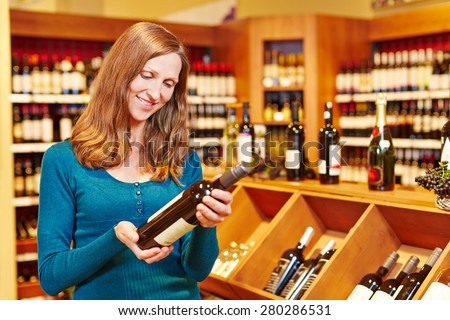 Elderly smiling woman buying bottle of red wine in a supermarket