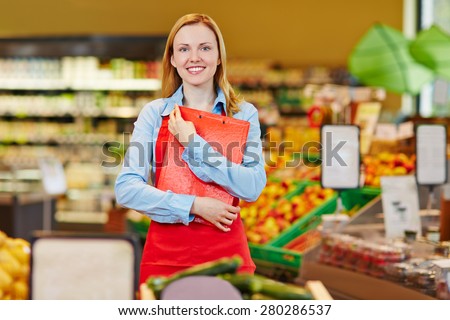 Smiling young saleswoman standing in supermarket with a checklist