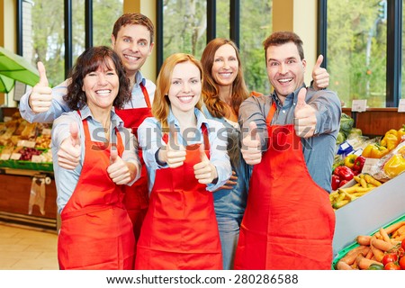 Happy staff team in a supermarket holding their thumbs up