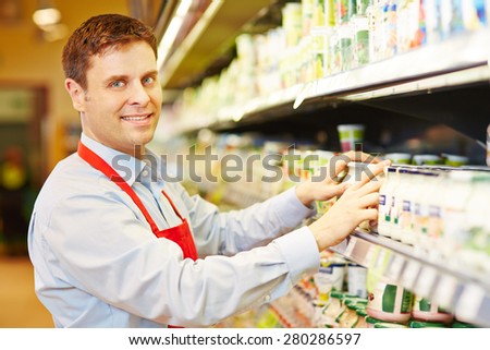 Smiling salesman organizing dairy products in supermarket shelf