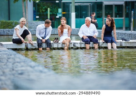 Happy business people talking during break in summer with their feet in water