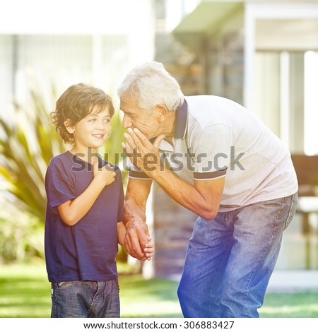 Grandfather whispering a secret in the ear of his grandson in a garden