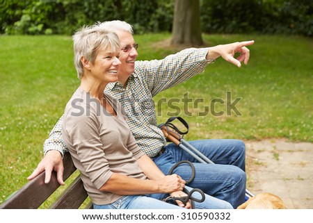 Happy senior couple on park bench pointing with finger into the distance