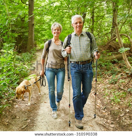 Two smiling seniors walking with their dog in a forest in summer