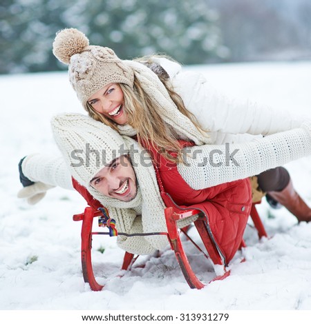Couple having fun while sledding on sled in winter