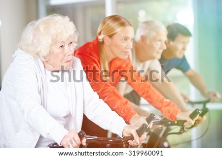 Old woman exercising in group on a spinning bike in gym