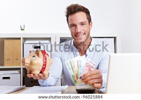 Happy business man with piggy bank and money in office