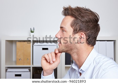 Young business man in profile view with hand on chin in office