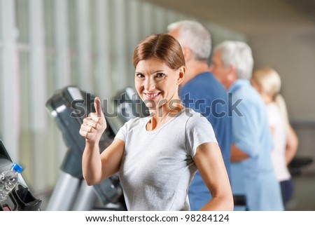 Smiling elderly woman on treadmill holding thumb up in fitness center
