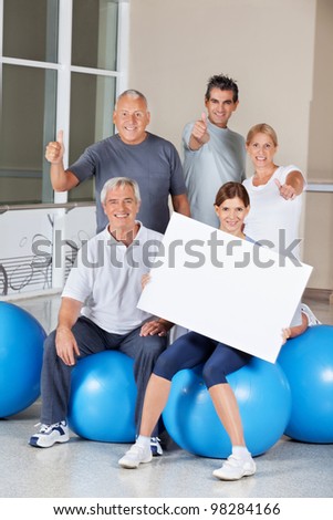 Senior citizens on gym balls holding empty advertising sign in fitness center