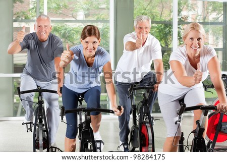 Senior group on bikes in gym holding thumbs up
