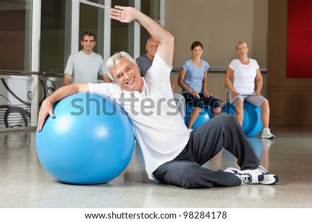 Elderly man doing back exercises with gym ball in fitness center