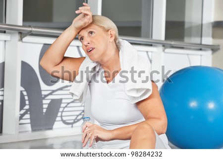 Tired senior woman wiping sweat of her forehead in gym