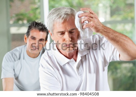 Senior man wiping sweat of his forehead with towel in gym