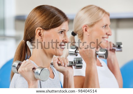 Two elderly women exercising with dumbbells in fitness center