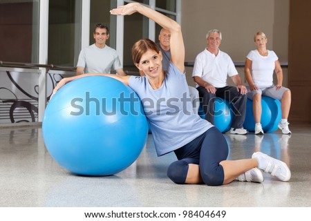 Happy woman doing back exercises with blue gym ball in fitness center