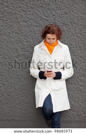 Young woman leaning on wall looking at her cell phone