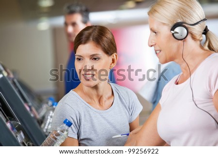 Fitness trainer talking to senior woman on treadmill in gym