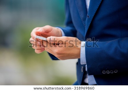 Handsome businessman in suit standing at the street with smart phone in hand. Modern skyscrapers on the background. Close-up