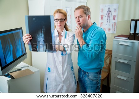Worried female doctor with handsome male patient looking at x-ray at office. Doctor talking to her patient and showing radiograph.