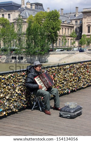 PARIS, FRANCE - MAY 23, 2013: An accordion player sitting on a bridge in Paris and plays French songs. Behind him is the bridge railing, full of thousands of love locks.