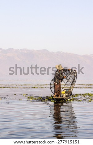 NIAUNGSHWE, MYANMAR - JANUARY 31, 2015: A fisherman at Inle lake iscatching fish in a big fish trap. In the background are the moutains