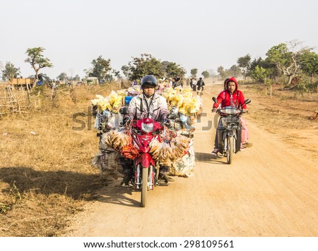 LOIKAW, MYANMAR - FEBRUARY 7, 2015: A street seller is driving his motorbike along a road near Loikaw, Myanmar. The bike is loaded with his merchandise.
