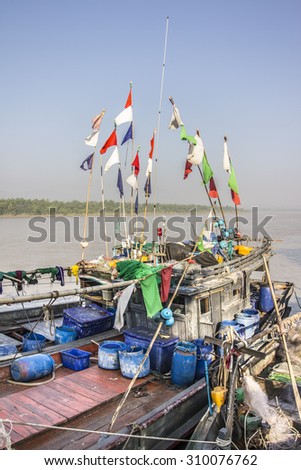 DAWEI, MYANMAR - FEBRUARY 16, 2015: A fisherboat on Tevoy river  at Dawei in the south of Myanmar, is lying at the pier. Colorful flags rise upwards.