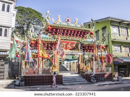 MYEIK, MYANMAR - FEBRUARY 23, 2015: The entrance to the chinese temple at Myeik in the south of Myanmar. A beautiful lady passes by in the foreground.