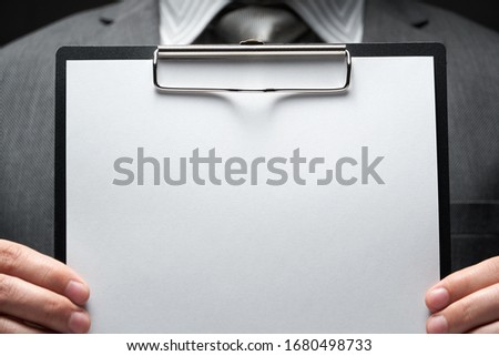 white blank paper sheet closeup in businessman hand, gray suit, dark wall background, blank space for text 商業照片 © 