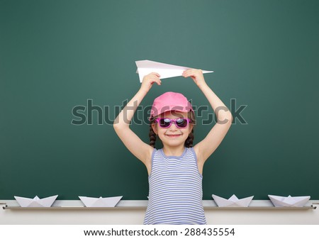 Girl near the school board with paper plane boat