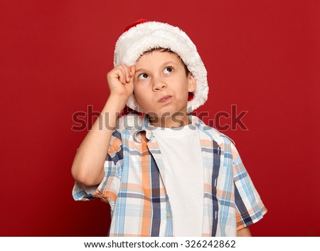 winter holiday christmas concept - boy in santa helper hat have idea on red background