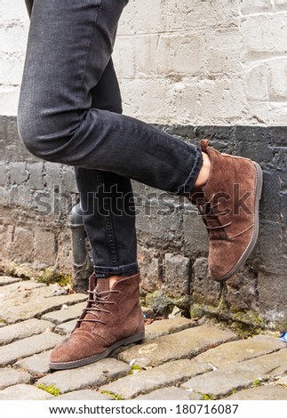 Model legs wearing tight black skinny trousers and brown ankle boots. Black and white brick wall as a background.