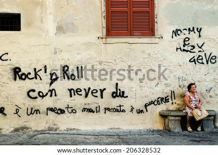 TROPEA, CALABRIA, ITALY, April 2014: Graffiti in an old Italian town in Calabria. Old woman sitting next to a wall with the words \