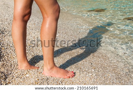 Legs of a tanned model with shadow projected on a pristine Mediterranean sea in Italy. Focus on legs and feet with red nail varnish.