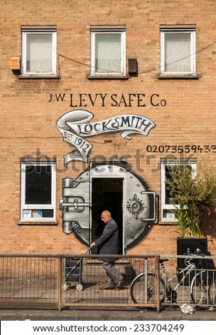 Shoreditch, London, UK, September 28 2014: Old man walking in front of a locksmith shop with a safe door drawn on the shop door.
