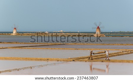Marsala, Sicily, Italy, July 26 2014: Two workers at the west coast salt pans in Marsala carrying and heavy load.