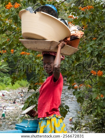 Santana, Sao Tome and Principe - 18 August 2014: A young girl dressed in traditional way, carrying dishes and clothes to be washed on her head.