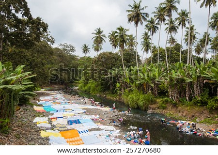 Santana, Sao Tome and Principe - 18 August 2014: African women washing clothes on a river. Washed clothes are lied down on the river shore to dry under the sun.