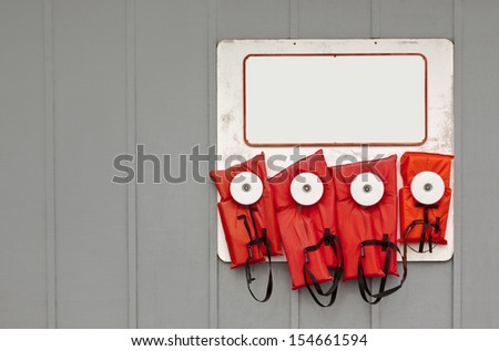 Life jackets have proven to save lives. Here are two adult, one adolescent, and one small child life jackets hanging on a wall with a whiteboard above them.