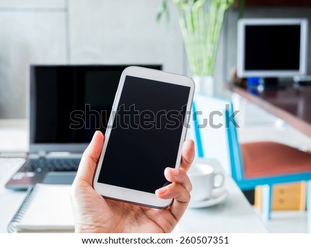 Hand holding mobile phone (cell phone) over modern workspace background