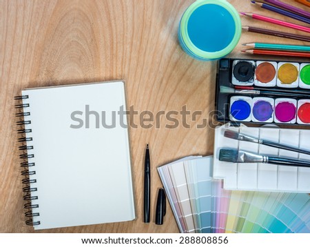 Top view of blank  sketchbook, watercolor paints, color-pencils for painting on  wooden background