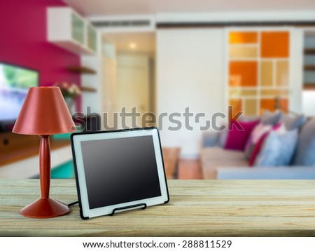 Red lamp, tablet on wooden table top with modern Living room blurry background