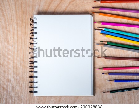 Top view of blank notebook with color-pencils on  wooden background/ artist drawing concept