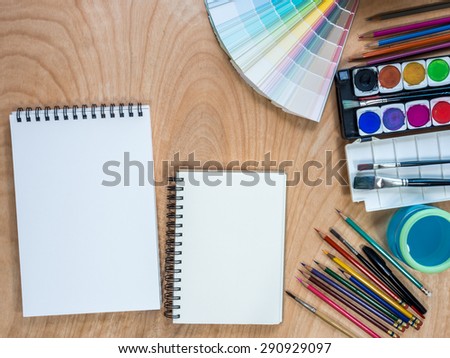 Top view of blank  sketchbooks, watercolor paints, color-pencils for painting on  wooden background
