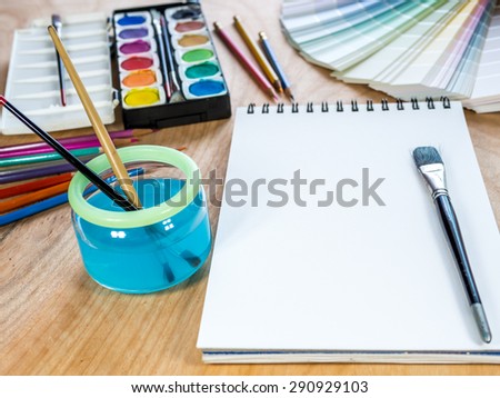 Blank  sketchbook,  brush, watercolor paints, color-pencils for painting on wooden table background